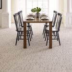A photo of multi-coloured carpet installed in a dining room. There is a wooden dining set in the middle of the room.